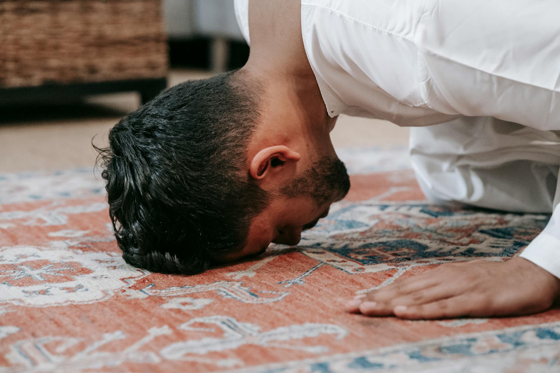 man in white thobe bowing down on red and blue rug